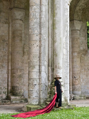 Fototapeta na wymiar Femme avec une étoffe se doie rouge dans les ruines d'une église du moyen age