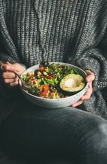 Healthy vegetarian dinner. Woman in grey jeans and warm sweater holding bowl with fresh salad, avocado, grains, beans, roasted vegetables. Superfood, clean eating, vegan, dieting food concept