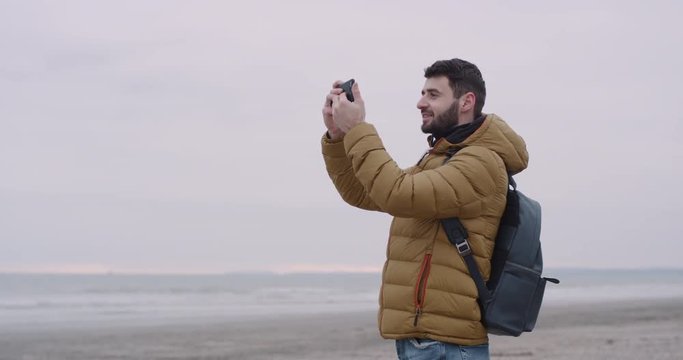Impressed man tourist take pictures with his phone , he arrived in nice place on a large beach with a sea view , walking people around