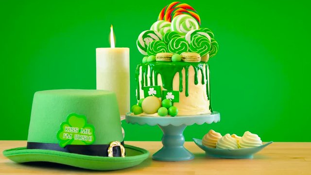 St Patrick's Day party table with lollipop candyland drip cake on green background.