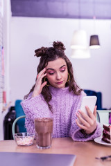 Skeptical long-haired girl in knitted sweater checking social medias