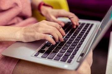 Young girl with golden accurate jewelry typing on her laptop keyboard