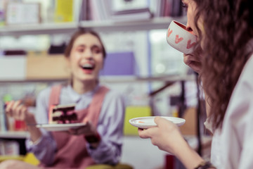 Laughing cheerful ladies drinking tea and eating dessert