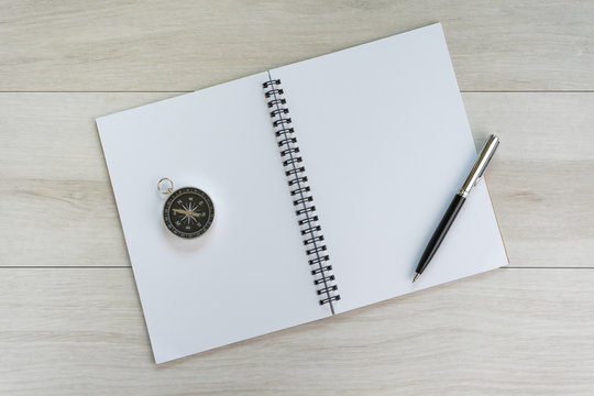 White opening blank paper note book with pen on the right and navigation compass on light grey wooden table background with copy space, world travel and direction concept - Powered by Adobe