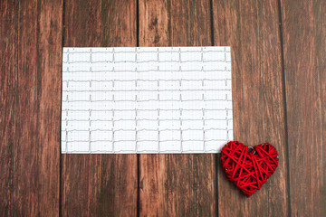 Cardiogram chart with small red heart on wood background.