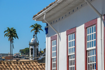 Detalhe de fachada de janelas de casa colonial de São João del Rey e, ao fundo, torre da Igreja...