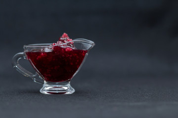 Home-made sweet raspberry jam in a glass sauce-boat on a black background