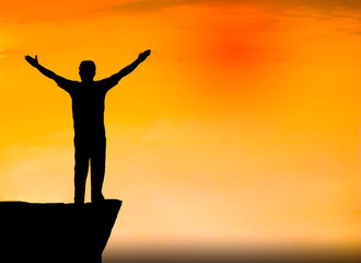 Fototapeta premium Silhouette photo. A man show hand and standing on cliff. A man happy and good feel for nature. He is see sun set. Photo concept achievement and lifestyle.