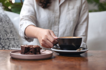 Fototapeta na wymiar Closeup image of a woman's hand holding and drinking hot latte coffee with brownie cake on the table