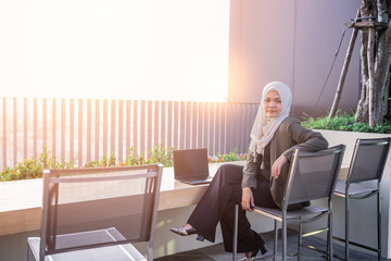 confident young asian muslim woman sitting office chair and working on outdoors. working concept.