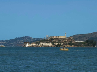 Fototapeta na wymiar a cute small yellow ferry sails past alcatraz island in san francisco