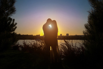 Silhouette of a loving couple on a sunset background. Romance at sunset time. The sun sets against the backdrop of the river and views of the city.