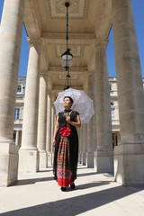Fototapeta na wymiar Femme avec ombrelle blanche en dentelle sous un portique du palais royal