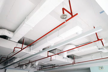 Perspective view of white air duct on the ceiling with red water sprinkler pipe - obrazy, fototapety, plakaty