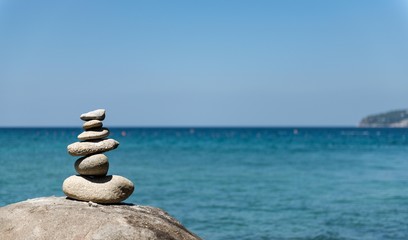 Fototapeta na wymiar Stones pyramid on pebble beach symbolizing stability, zen, harmony, balance. Shallow depth of field