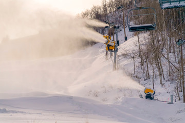 Snow cannons and ski lifts on snowy mountain slope