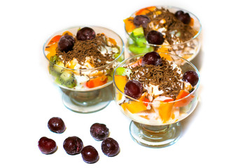 Сitrus fruit salad in a glass jar with milk cream and grated chocolate and frozen cherries. Оn a white background.