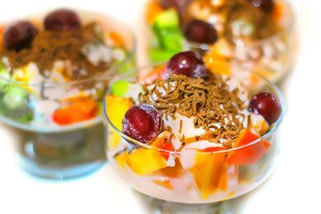 Сitrus fruit salad in a glass jar with milk cream and grated chocolate and frozen cherries. Оn a white background.