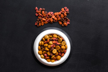 Dog food. Dry food in shape of bone near bowl on black backgorund top view copy space