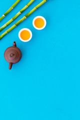Asian tea traditions. Drink tea. Tea ceremony. Tea pot near cups of green tea and bamboo decoration on blue background top view space for text