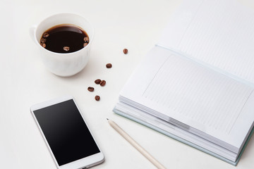 White office desk with blank diary or planner, pencil, phone and cup of coffee. Light background