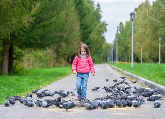 Child is playing with pigeon birds at city garden, lot of doves on path in public park