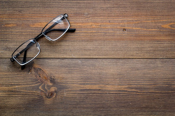 Stylish glasses with transparent lenses on dark wooden background top view space for text