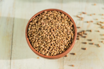 Dry buckwheat in brown clay bowl on wooden table. gluten free grain for healthy diet