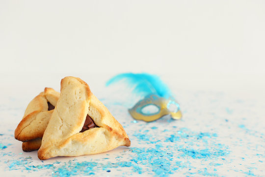 Purim celebration concept (jewish carnival holiday). Traditional hamantaschen cookies with mask over white wooden table