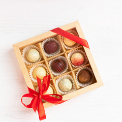 A gift set of various candies in a crafting box is decorated with a red satin ribbon. Festive concept. Flat layout.