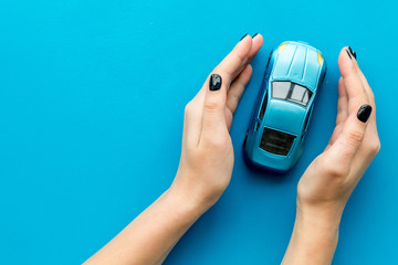 Car insurance concept. Safety of auto. Car toy in female hands on blue background top view copy space