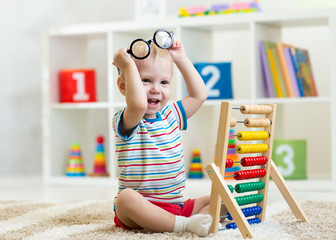 child boy with eyeglasses playing abacus toy in nursery