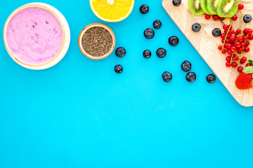 Preparing healthy fruit smoothie. Acai smoothie bowl near cutting board with fresh fruits, berries, chia seeds on blue background top view copy space