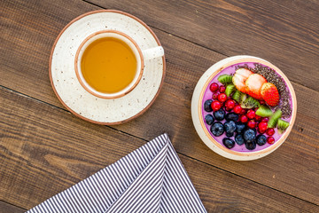 Light breakfast or healthy snack. Acai smoothie bowl with fresh fruits, berries, chia seeds on dark wooden background top view