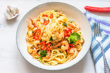 Pasta with shrimps, parsley and chilli peppers on a plate, on a light wooden background - traditional Mediterranean linguine with seafood, Italian cuisine. - obrazy, fototapety, plakaty