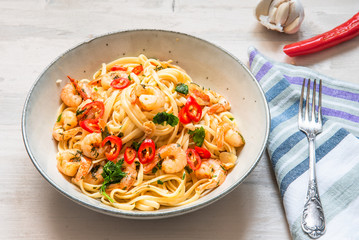 Pasta with shrimps, parsley and chilli peppers on a plate, on a light wooden background - traditional Mediterranean linguine with seafood, Italian cuisine.