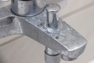Close-up of shower mixer faucet with limescale, white chalky deposit and stains. Formed on the...