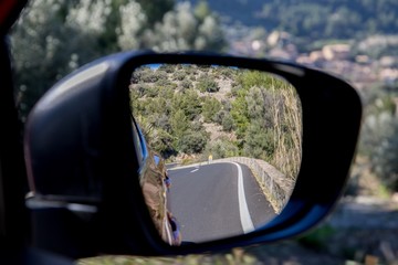 Car driving travel concept - car rear view mirror view of a mountain road with rocks and trees 