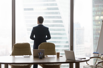 Rear view at successful businessman standing back in modern office