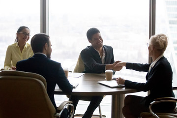 Smiling executive businesswoman handshaking african businessman at group meeting