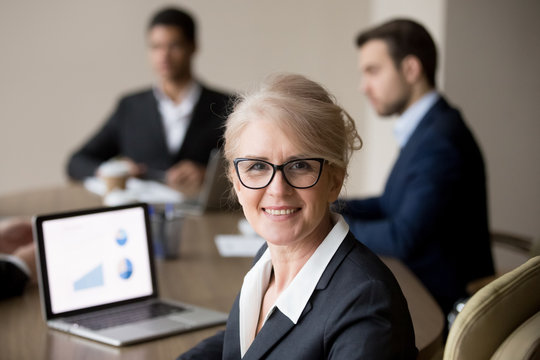 Happy middle-aged businesswoman in glasses posing at team office meeting