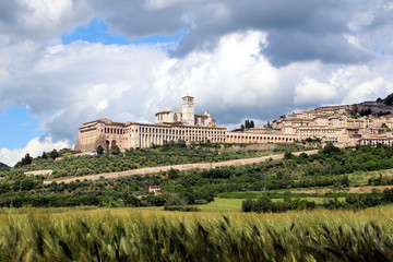 Fototapeta na wymiar Assisi, Umbria, Italy. Panorama of the hill of the city seen from a hay field in the plain. on the left the cathedral of San Francesco.