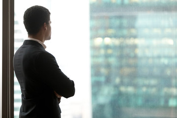 Rear view of successful african businessman standing looking at window