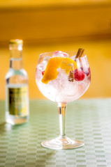 Cocktail de gin tonic de twist de naranja, frambuesas y canela y botella de tónica en el fondo desenfocado