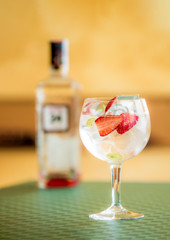 Cóctel de gintonic de gin y tónica con fresas y uva, botella de ginebra en desenfoque en el fondo