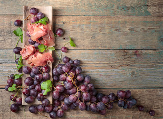 Prosciutto with parsley and grapes on a old wooden table .