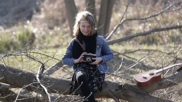 The girl in the park takes pictures with an old-fashioned camera. A dreamy teenager in the park is playing with an old photographic camera