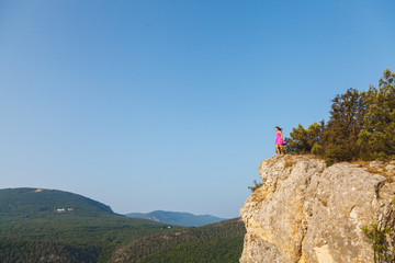 A girl in a pink dress stands on a rock in front of a precipice
