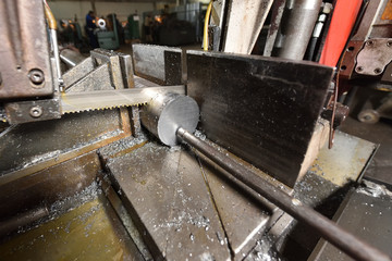 The process of cutting metal with an electric saw in a factory. Electric saw cuts round metal