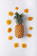 Dried pineapple rings and whole fresh pineapple on white background. Top view, flat lay.